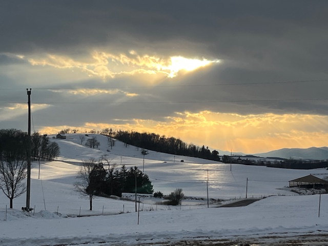 Snowy landscape with sun peeking through a small opening in the clouds.